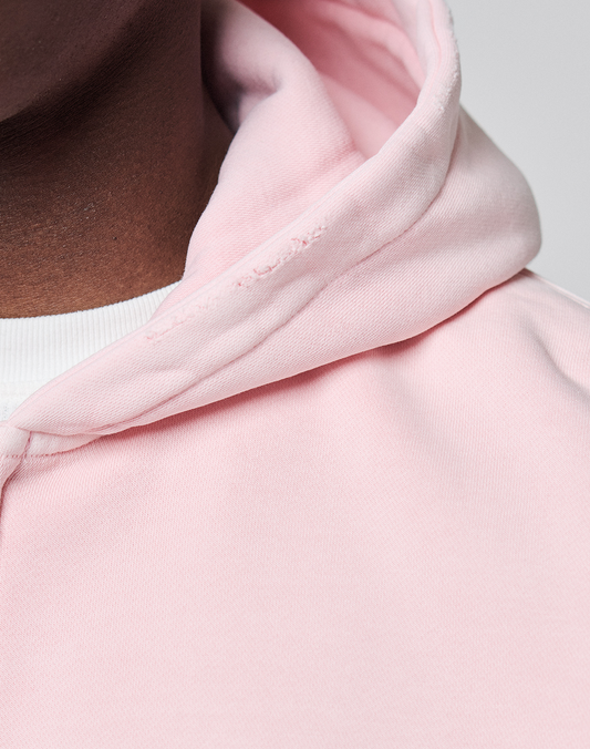 Close-up of a person wearing the LIVE FAST DIE YOUNG Basic Evidence Hooded Zip in light pink over a white shirt. The image highlights the fabric, seam details, and branding on this oversize fit hoodie with part of their neck visible.