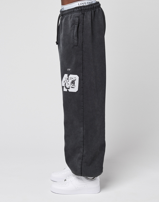 A person wears black LFDY 40 Wide Cuff Joggers by LIVE FAST DIE YOUNG with an oversize fit, side pockets, white '40' and tiger graphic, and a white LIVE FAST waistband, paired with white sneakers, standing sideways against a plain background.