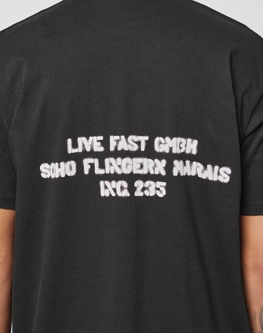 The LFDY District Tee by LIVE FAST DIE YOUNG is a black cotton shirt with white, distressed "LIVE FAST GMBH SOHO FLINGERN MARAIS INC. 235" text on the back, printed front and back in regular fit for a vintage, faded look.