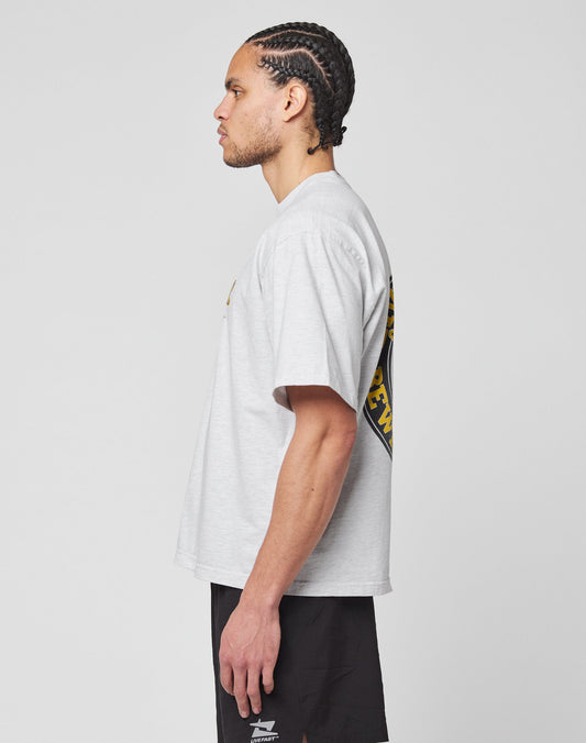 A man with cornrow braids stands in profile against a plain white background, wearing the LIVE FAST DIE YOUNG LFDY Circle Dog Tee in an oversize fit and black athletic shorts.