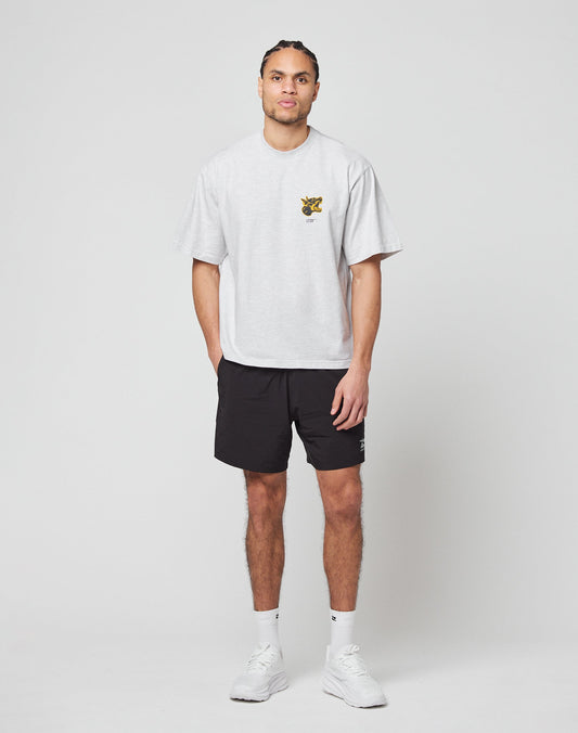 A man stands against a plain white background wearing the LIVE FAST DIE YOUNG LFDY Circle Dog Tee in light gray, oversize fit with a small chest graphic, black shorts, white socks, and white sneakers. He looks straight ahead with his hands at his sides.