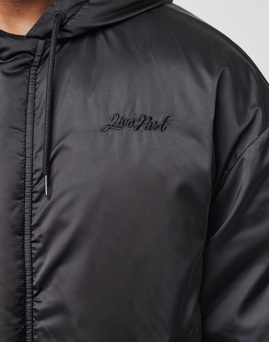 Close-up of the LFDY Winter Bomber Jacket by LIVE FAST DIE YOUNG, featuring a black hood with drawstrings and Live Fast embroidered in black script on the chest. Only part of the model in this Oversize Fit style is visible.