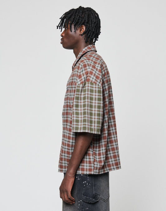 A person with short, twisted hair models the LIVE FAST DIE YOUNG LFDY Light Flannel—an oversize fit, short-sleeve plaid shirt with mismatched brown and green sleeves—paired with dark jeans against a plain light background.