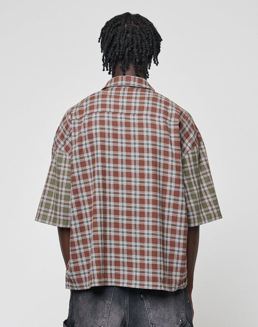 A person with short, twisted hair is seen from behind wearing the LIVE FAST DIE YOUNG LFDY Light Flannel—an oversized, short-sleeved plaid shirt in brown and green—paired with dark denim shorts against a plain background.