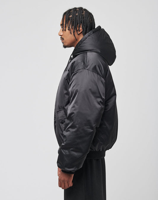 A man with braided hair, wearing an oversized black LFDY Winter Bomber Jacket by LIVE FAST DIE YOUNG and black pants, stands facing sideways against a plain white background.