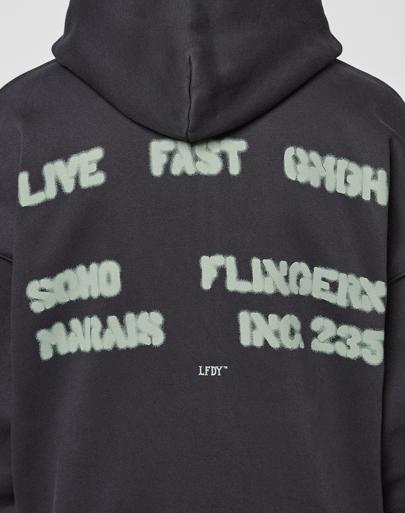 The Live Fast District Hooded Zip by LIVE FAST DIE YOUNG is a black oversized hoodie featuring white spray-painted text: “LIVE FAST DIE YOUNG,” “SOHO,” “MARIA’S,” “FLINGERX,” and “INC. 235.” LFDY branding appears on the upper back.
