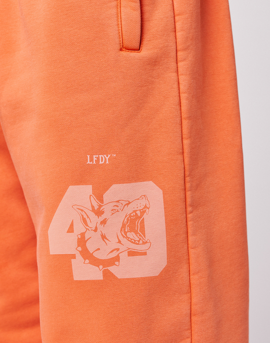 Close-up of the LFDY 40 Wide Cuff Jogger by LIVE FAST DIE YOUNG in orange Oversize Fit, featuring a printed 43, snarling dog graphic with spiked collar, LFDY text above, and side pockets.