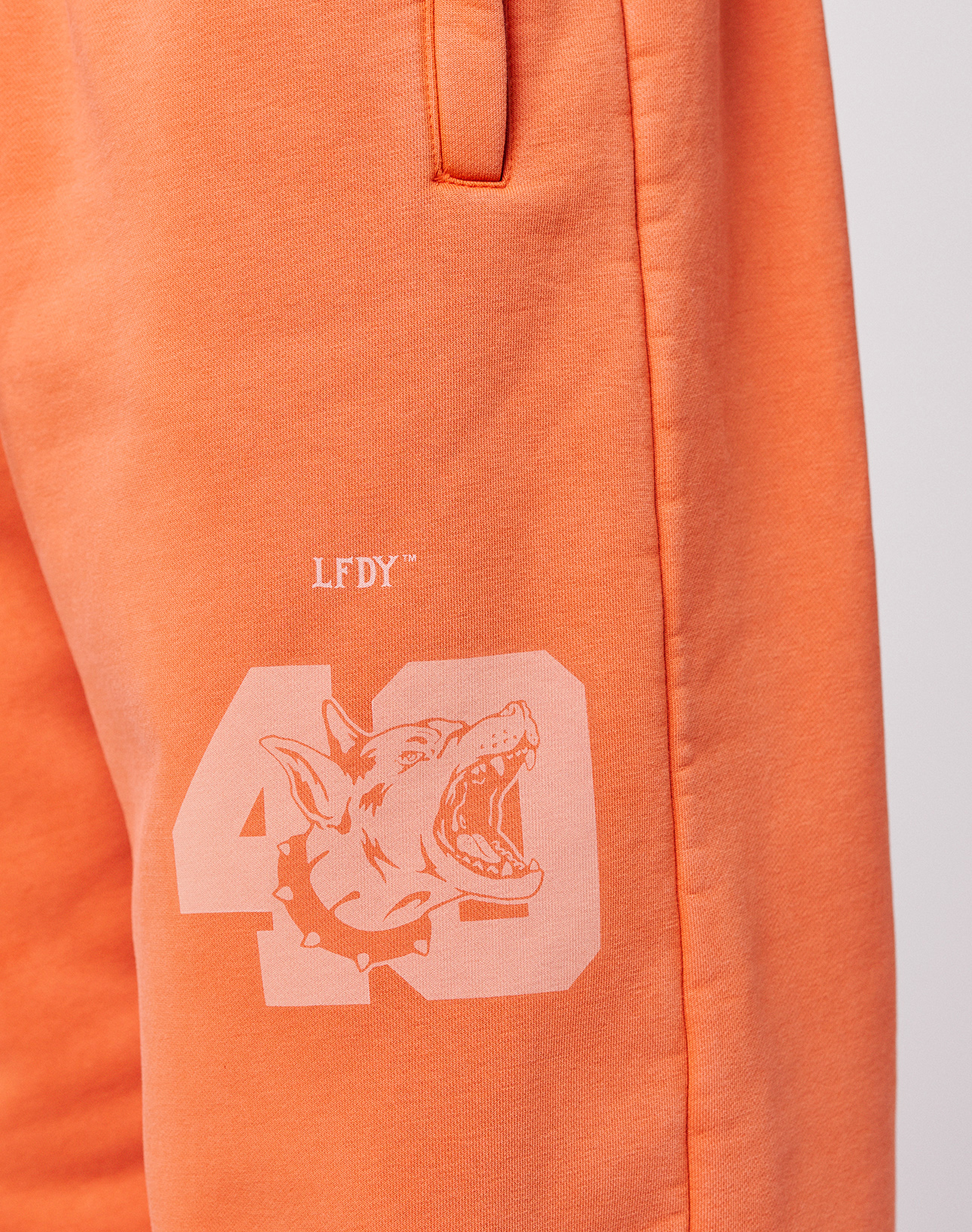 Close-up of the LFDY 40 Wide Cuff Jogger by LIVE FAST DIE YOUNG in orange Oversize Fit, featuring a printed 43, snarling dog graphic with spiked collar, LFDY text above, and side pockets.