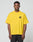 A man stands facing forward wearing the LFDY Circle Dog Tee by LIVE FAST DIE YOUNG, a loose-fitting yellow oversize t-shirt with a small black LFYT graphic on the upper left chest, made from 100% cotton, paired with black pants against a light gray background.