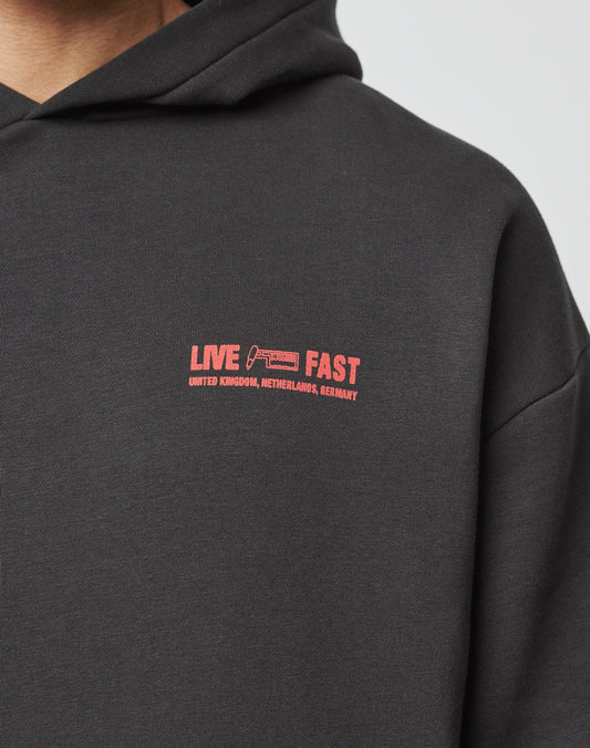 A close-up of the Hit and Run Hooded by LIVE FAST DIE YOUNG, an oversized black hoodie with a discharge front print: bold red LIVE FAST text, UNITED KINGDOM, NETHERLANDS, GERMANY below, plus a small car graphic for added style and comfort.