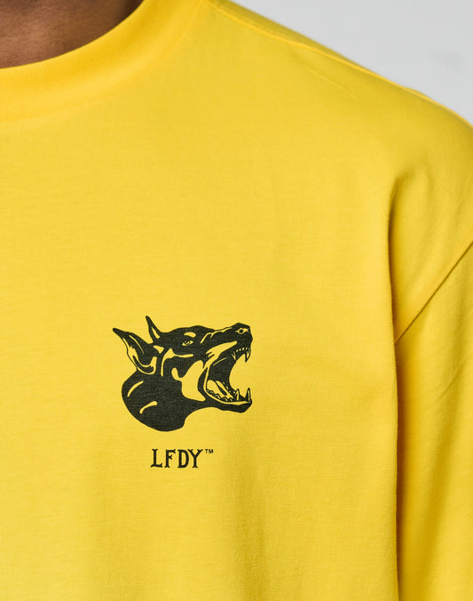 The LFDY Circle Dog Tee by LIVE FAST DIE YOUNG is a yellow oversized shirt with a vintage wash, showcasing a black snarling dog graphic and LFDY text printed below on the chest.