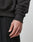 A close-up of a person’s left hand and wrist, wearing black textured pants and the oversized Hit and Run Hooded sweatshirt by LIVE FAST DIE YOUNG, featuring ribbed fabric and a small fabric tag near the waistband.