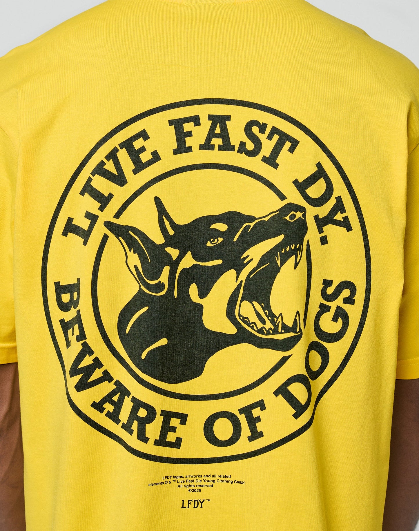 The LFDY Circle Dog Tee by LIVE FAST DIE YOUNG is a yellow Oversize Fit shirt with a bold black snarling dog graphic and “LIVE FAST DY. BEWARE OF DOGS” text, made from 100% Baumwolle for comfort.