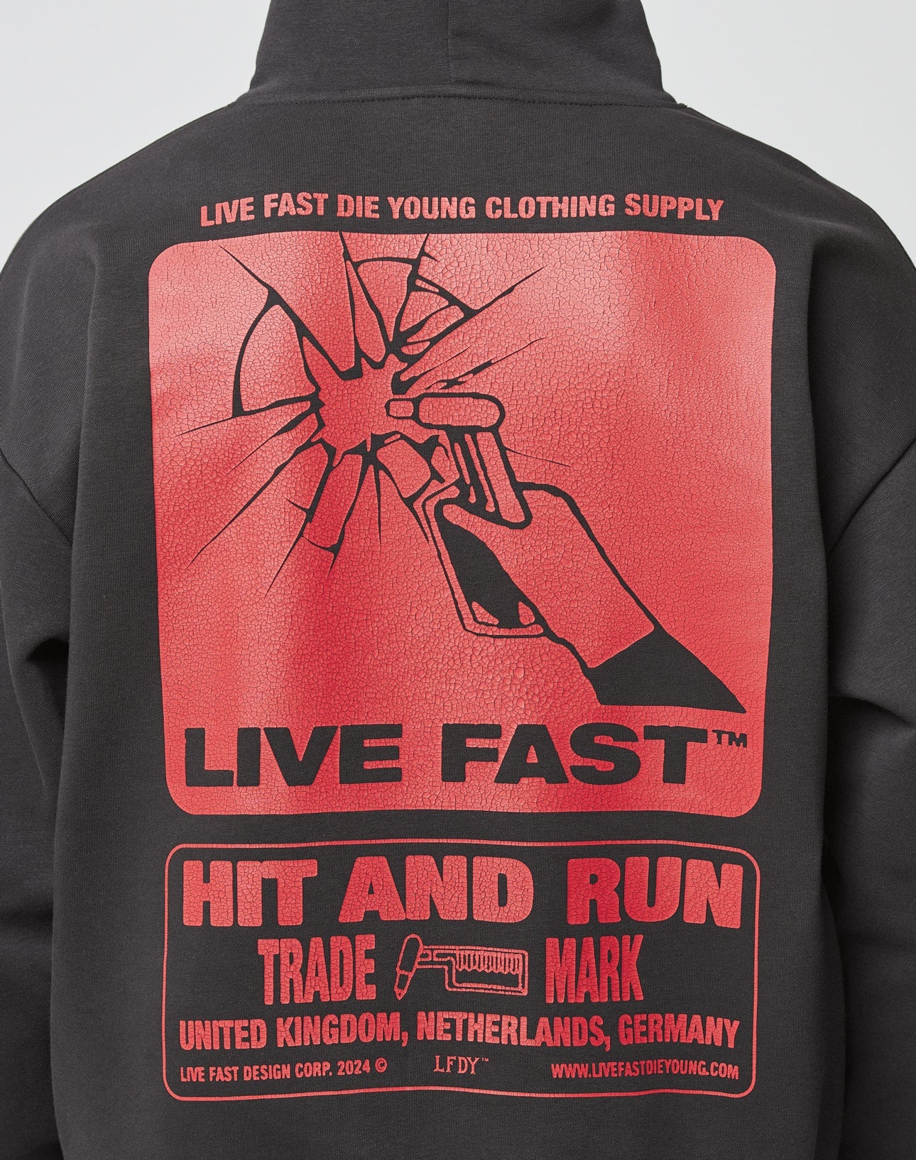 The Hit and Run Hooded by LIVE FAST DIE YOUNG is a black oversized hoodie with a large red cracked hand-and-crowbar backprint, featuring LIVE FAST, HIT AND RUN and locations: United Kingdom, Netherlands, Germany.