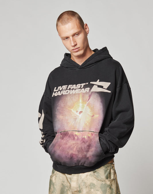 Someone in an oversize-fit LFDY Angel Hooded by LIVE FAST DIE YOUNG, featuring a cosmic graphic and LIVE FAST HARDWEAR text, pairs it with light tie-dye pants while standing against a plain background.