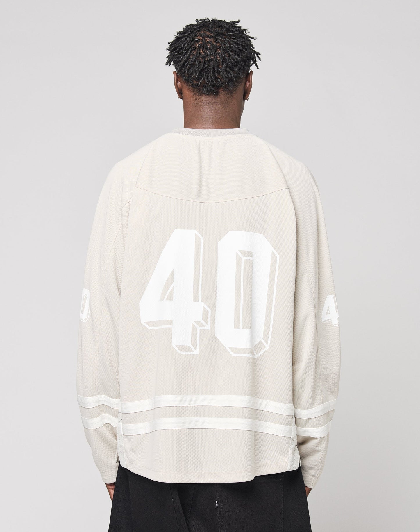 A person with short, twisted hair faces away, wearing an oversize light beige LFDY Hockey Jersey by LIVE FAST DIE YOUNG with the number 40 on the back and sleeves. The background is plain, light gray.