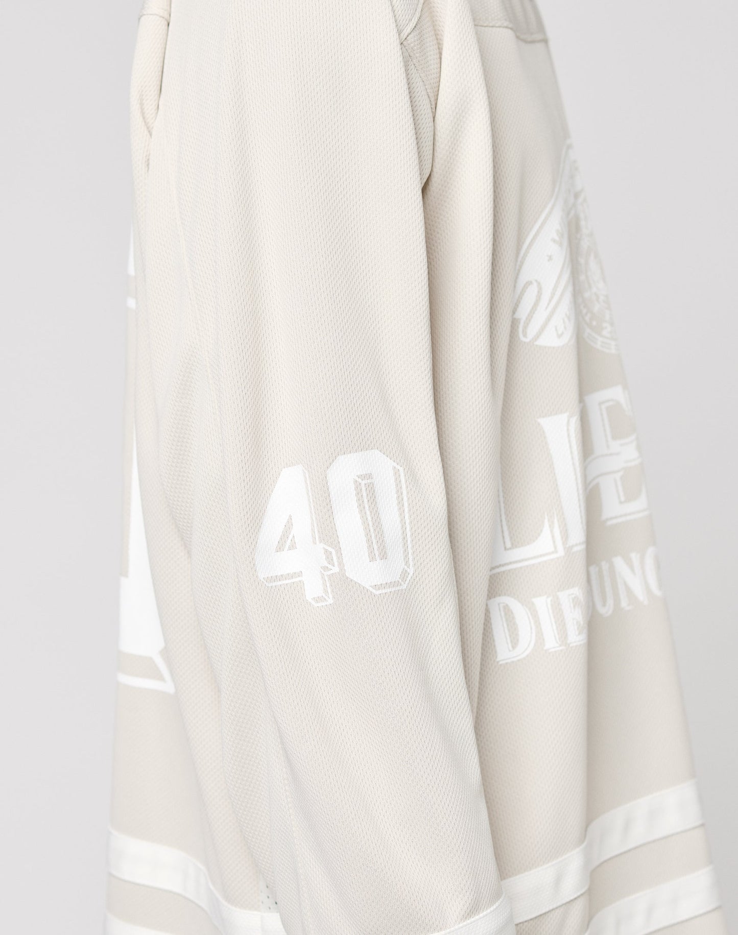 A close-up shows part of the upper body wearing the LFDY Hockey Jersey by LIVE FAST DIE YOUNG in light beige, featuring a number 40 Ärmelprint, white lettering, textured polyester fabric, and an oversized fit.
