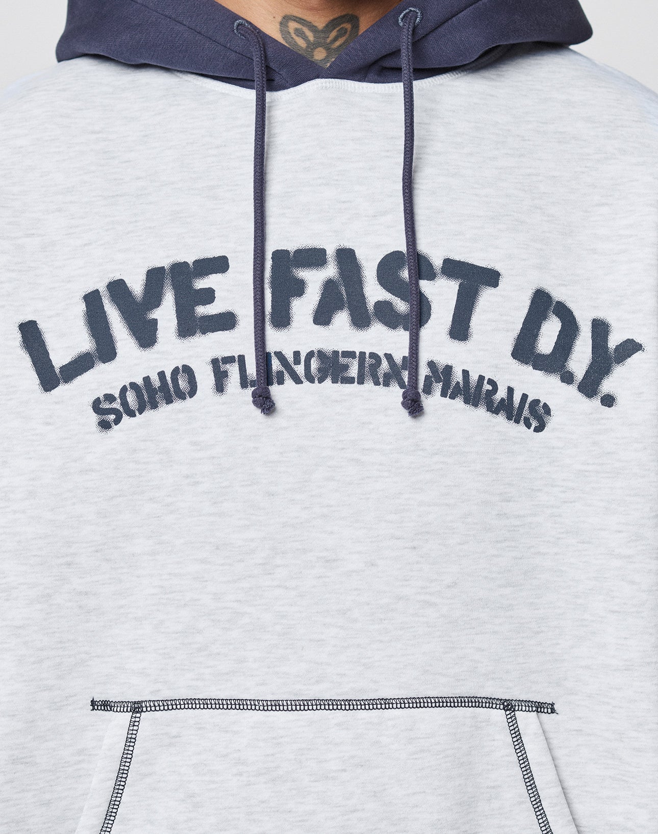 Close-up of a person wearing a light gray LFDY District Hooded by LIVE FAST DIE YOUNG, featuring dark blue drawstrings and hood. "LIVE FAST D.Y. SOHO FUNGERIN MARAIS" is boldly printed on the front.