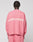 Seen from behind, a person with short braided hair wears the LIVE FAST DIE YOUNG "Live Fast Boucle Sweater," an oversized pink knit with "LIVE FAST" in white on the back, paired with matching pink pants against a plain light background.