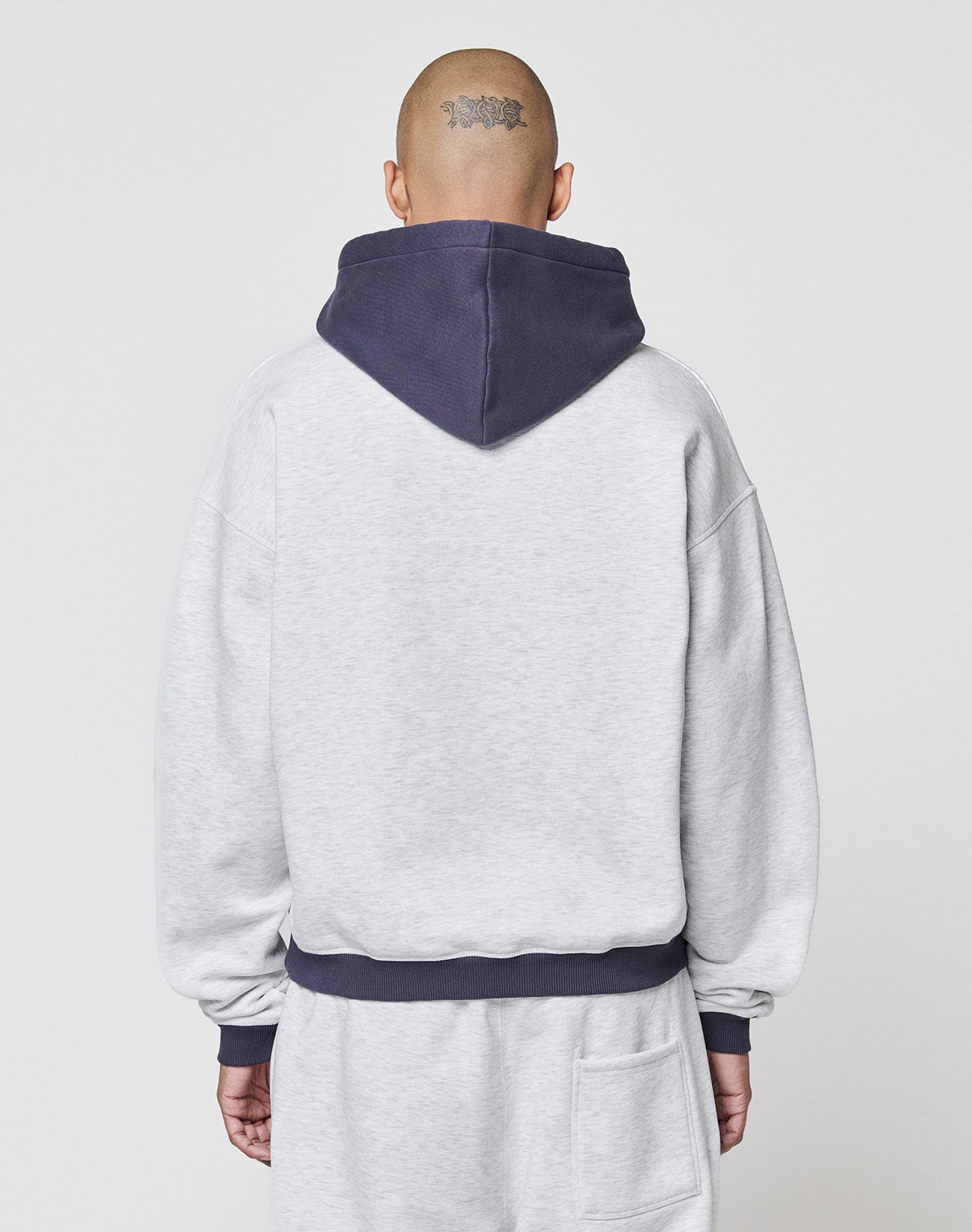 A person with a shaved head and a tattoo on the back wears the LFDY District Hooded by LIVE FAST DIE YOUNG in light gray with contrast hood and cuffs, shown from behind against a plain light background.