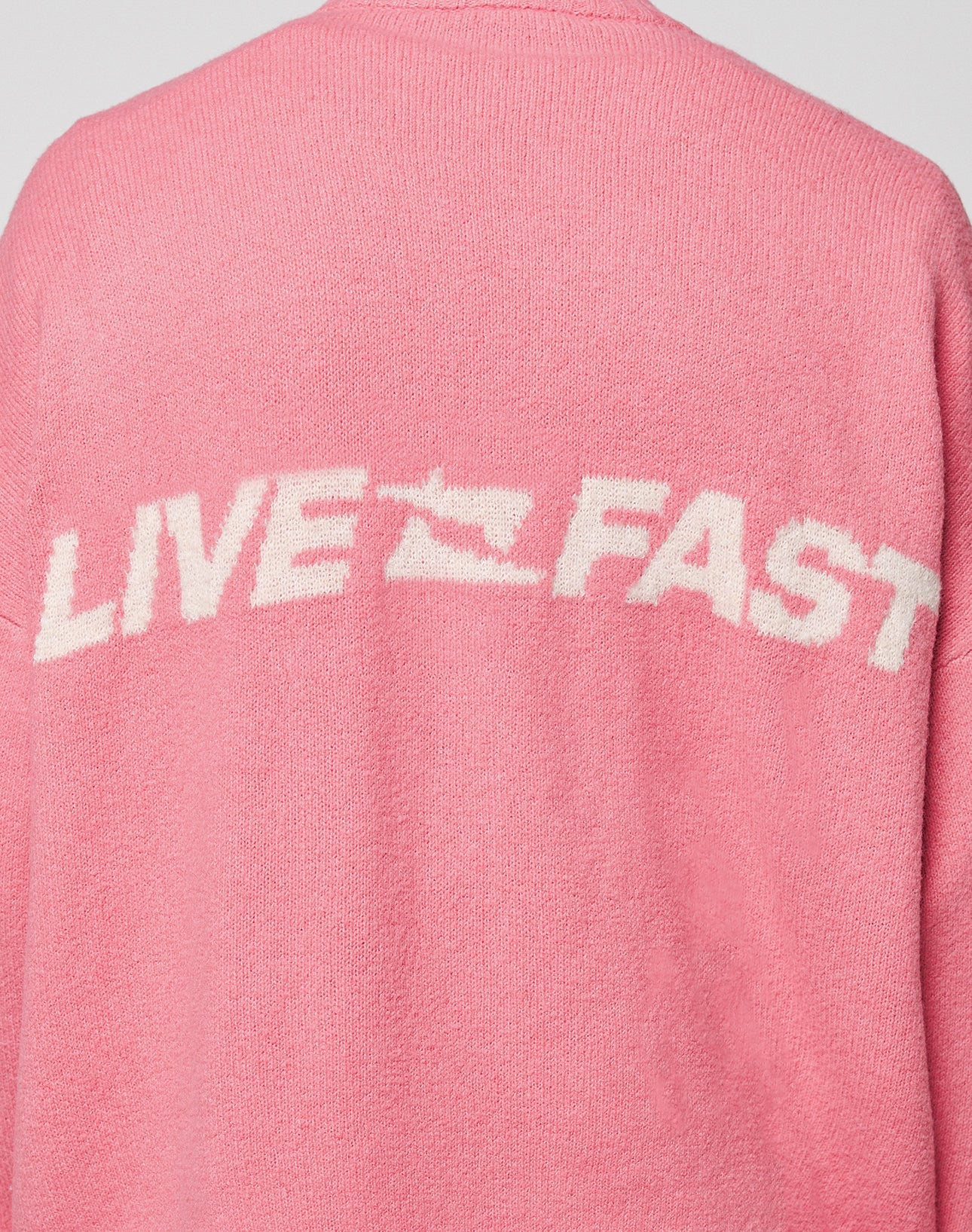 The LIVE FAST DIE YOUNG Live Fast Boucle Sweater is an oversized pink knit with "LIVE FAST" in bold white letters across the back, separated by a small running shoe graphic.