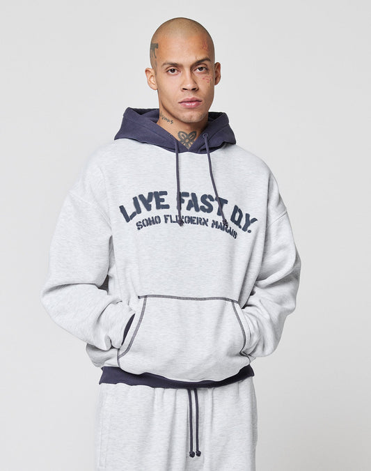A person with a shaved head wears the LFDY District Hooded by LIVE FAST DIE YOUNG in light gray with contrast trim and the words LIVE FAST D.Y. SOHO FLUCREHX MAHAL printed on the front, against a plain light background.