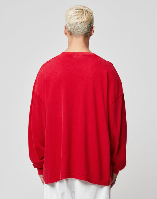 A person with short, bleached blonde hair is seen from behind wearing an oversize fit red LIVE FAST DIE YOUNG Ripped College Longsleeve and white pants against a plain light gray background.