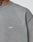 Close-up of a person wearing the grey Basic Trademark Tee by LIVE FAST DIE YOUNG, with small white LFDY™ embroidery on the chest. Part of the persons neck and a tattoo are partially visible.
