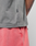 Close-up of a person wearing the LIVE FAST DIE YOUNG Basic Trademark Tee in grey, featuring a small black 1447 tag, paired with pink shorts. Hand in pocket and forearm tattoo visible for a unique look.