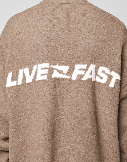 A close-up of the back of a brown Live Fast Boucle Sweater by LIVE FAST DIE YOUNG in Oversize Fit, featuring "LIVE FAST" in bold white lettering across it.