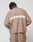 A person with short dreadlocks faces away, wearing the oversized brown LIVE FAST DIE YOUNG "Live Fast Boucle Sweater." The back of the sweater has bold white "LIVE FAST" text and a stylized graphic between the words.