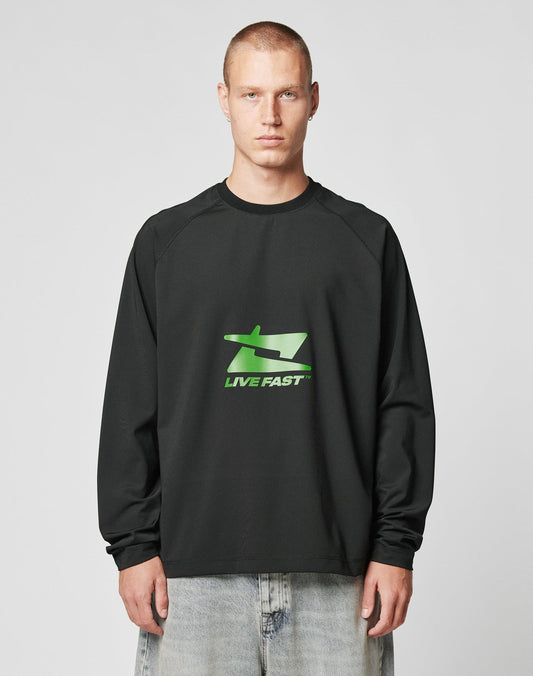 A person with short hair wears the black LFDY Sports Longsleeve by LIVE FAST DIE YOUNG, featuring a green LIVE FAST graphic, paired with light blue jeans against a plain light background. | model