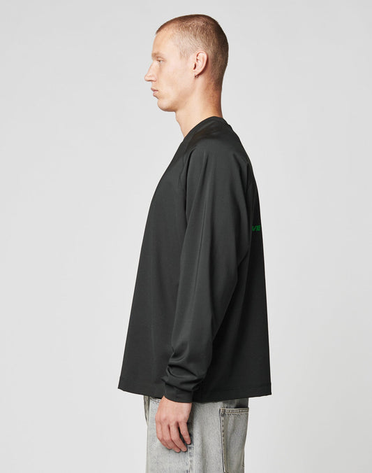 A man with short hair stands in profile facing left, wearing a black LFDY Sports Longsleeve by LIVE FAST DIE YOUNG and light gray jeans against a plain light background.