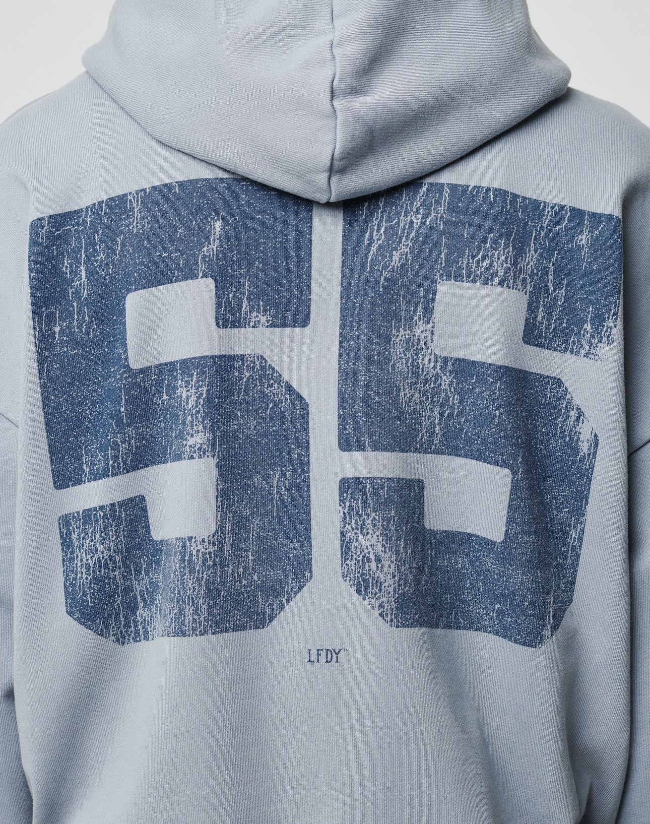 A close-up of the back of the LIVE FAST DIE YOUNG LFDY 55 Hooded Zip in light blue Oversize Fit, with a large distressed navy number 55 and small LFDY below, finished in vintage-washed cotton.