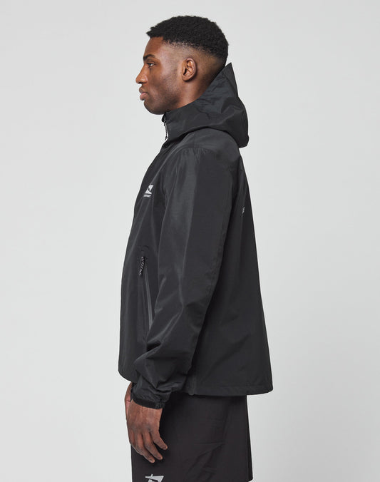 A man in a black LIVE FAST DIE YOUNG Live Fast Performance Rain Jacket with visor hood and black shorts stands in profile against a plain light gray background.