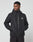 A man wears the Live Fast Performance Rain Jacket by LIVE FAST DIE YOUNG, featuring a black zip-up design, regular fit, elastic cuffs, and a white chest logo, standing with hands in pockets and looking left against a plain light background.
