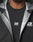 Close-up of a person wearing the black Live Fast Performance Rain Jacket by LIVE FAST DIE YOUNG, featuring Elastische Ärmelöffnung and partially unzipped to reveal a black shirt with the LIVE FAST logo and arrow design.