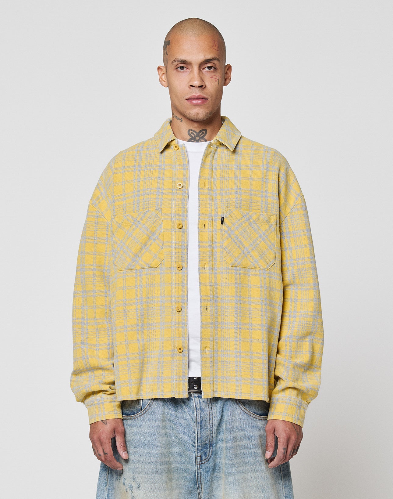 A person wears the LIVE FAST DIE YOUNG Vintage Flannel in yellow and gray plaid (Oversize Fit) over a white t-shirt and light blue jeans, standing facing forward against a plain white background.