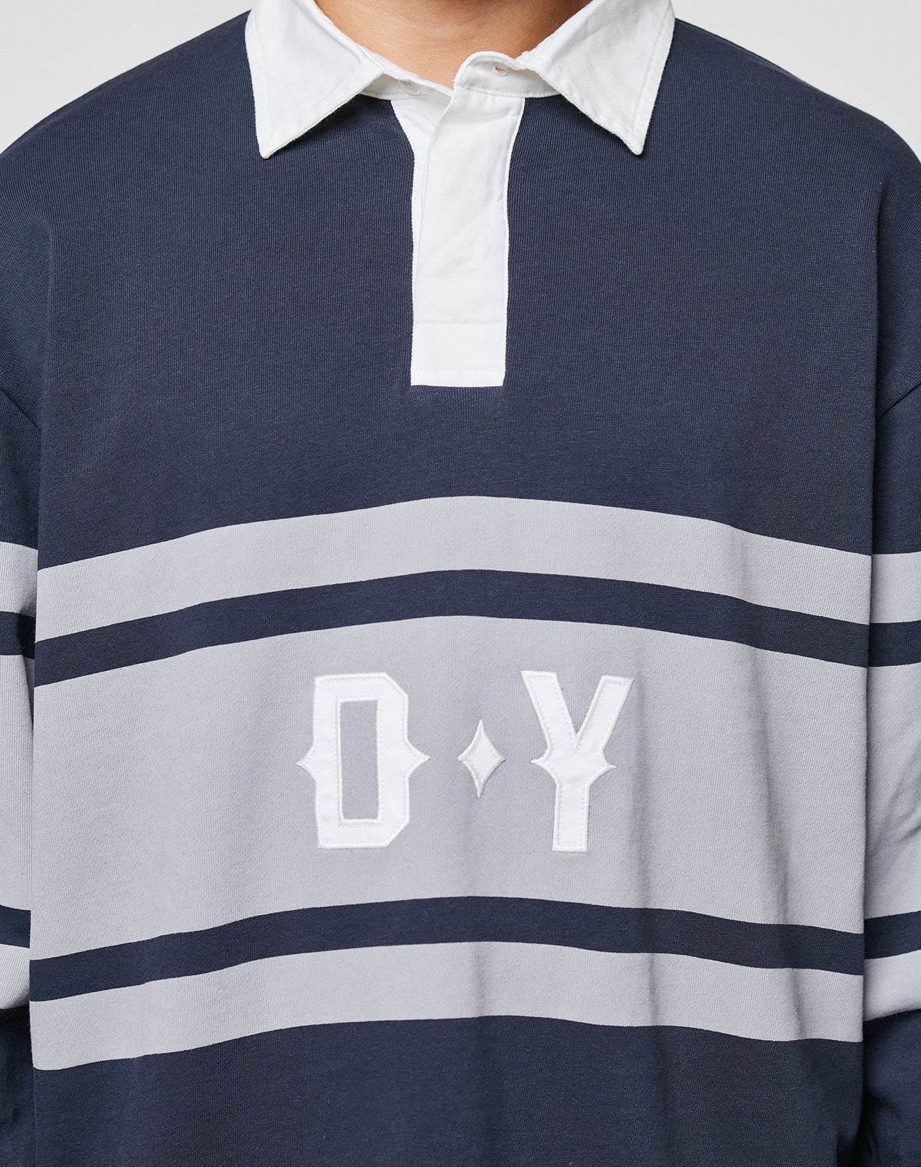 A person wearing the LFDY Striped Polo by LIVE FAST DIE YOUNG, featuring navy blue and gray stripes, a white collar, and D Y embroidered on the front. The image is cropped to display only the upper torso.
