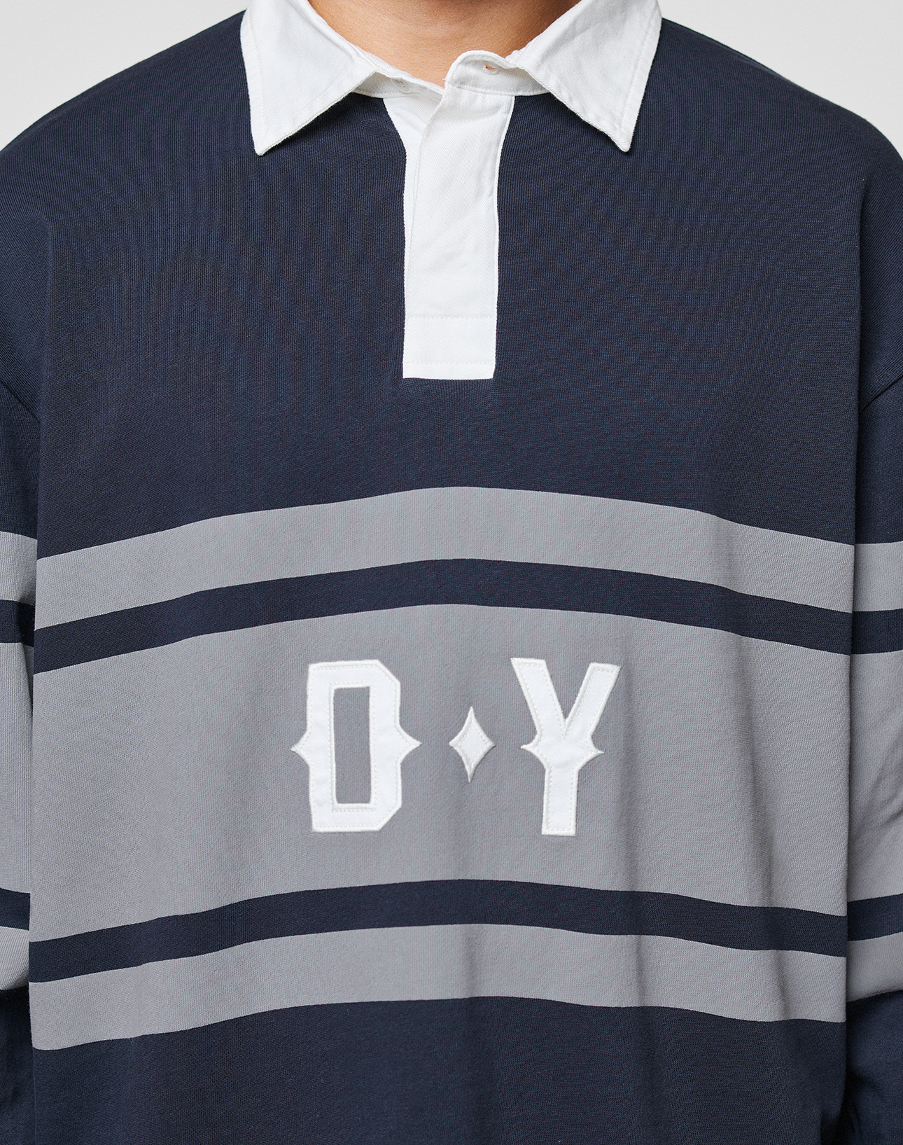 A person wears the LFDY Striped Polo from LIVE FAST DIE YOUNG, featuring navy and gray stripes, a white collar with button placket, and large white "O Y" letters on the front. The person's face is not shown.