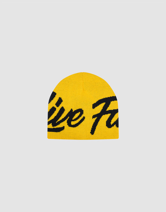 The LFDY Jacquard Beanie by LIVE FAST DIE YOUNG is a yellow Polyacryl knit hat with bold black cursive "Logo Strick" lettering across the front, shown on a plain light gray background. 
