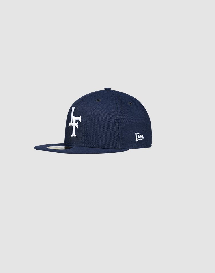 The LFDY x New Era 59Fifty Paris fitted cap by LIVE FAST DIE YOUNG features a navy blue color, flat brim, white LF logo on the front, New Era side embroidery, and is shown on a light gray background. Größentabelle available for sizing.