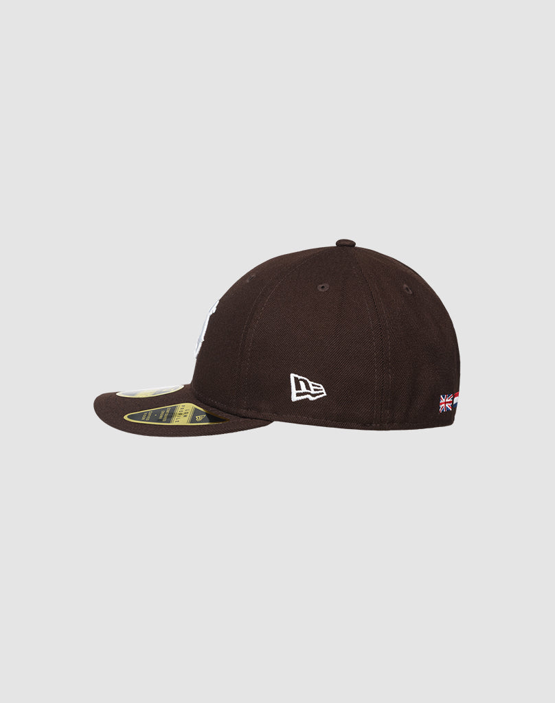 The LFDY X NEW ERA 59FIFTY LOW PROFILE by LIVE FAST DIE YOUNG is a black baseball cap with a curved brim and stickers, a white side logo, and a small flag above the adjustable back strap.