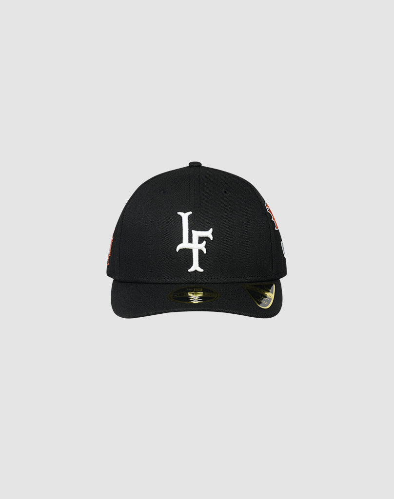 The LFDY X NEW ERA 59FIFTY LOW PROFILE by LIVE FAST DIE YOUNG is a black fitted cap with a white LF logo embroidered on the front, shown against a plain light gray background. A sticker appears on the low profile brim.| plain