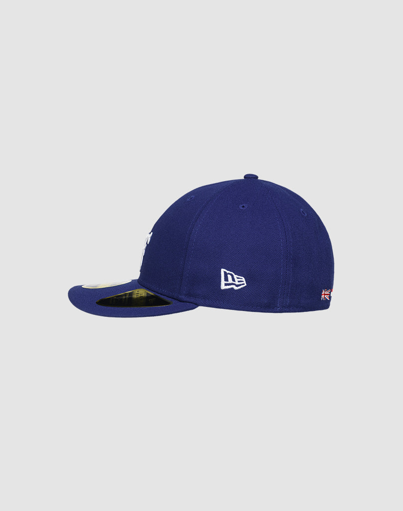 The LFDY X NEW ERA 59FIFTY LOW PROFILE by LIVE FAST DIE YOUNG is a navy blue fitted cap with a white embroidered logo on the side panel and a gold sticker on the flat brim, shown from the side.