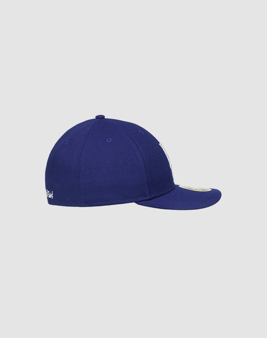 The LFDY X NEW ERA 59FIFTY LOW PROFILE fitted cap by LIVE FAST DIE YOUNG is shown from the side, with a flat brim, low-profile silhouette, and visible top stitching on a plain light gray background.