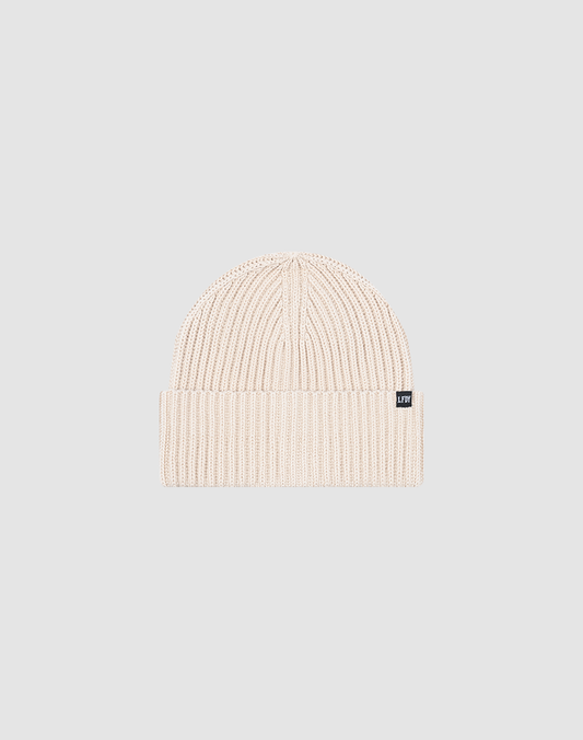 The LIVE FAST DIE YOUNG Rib Knit Beanie in light beige features a ribbed knit, folded brim with a black and white Flag-Label, and is made from a durable, comfortable polyamide blend. Shown on a plain gray background. One Size.