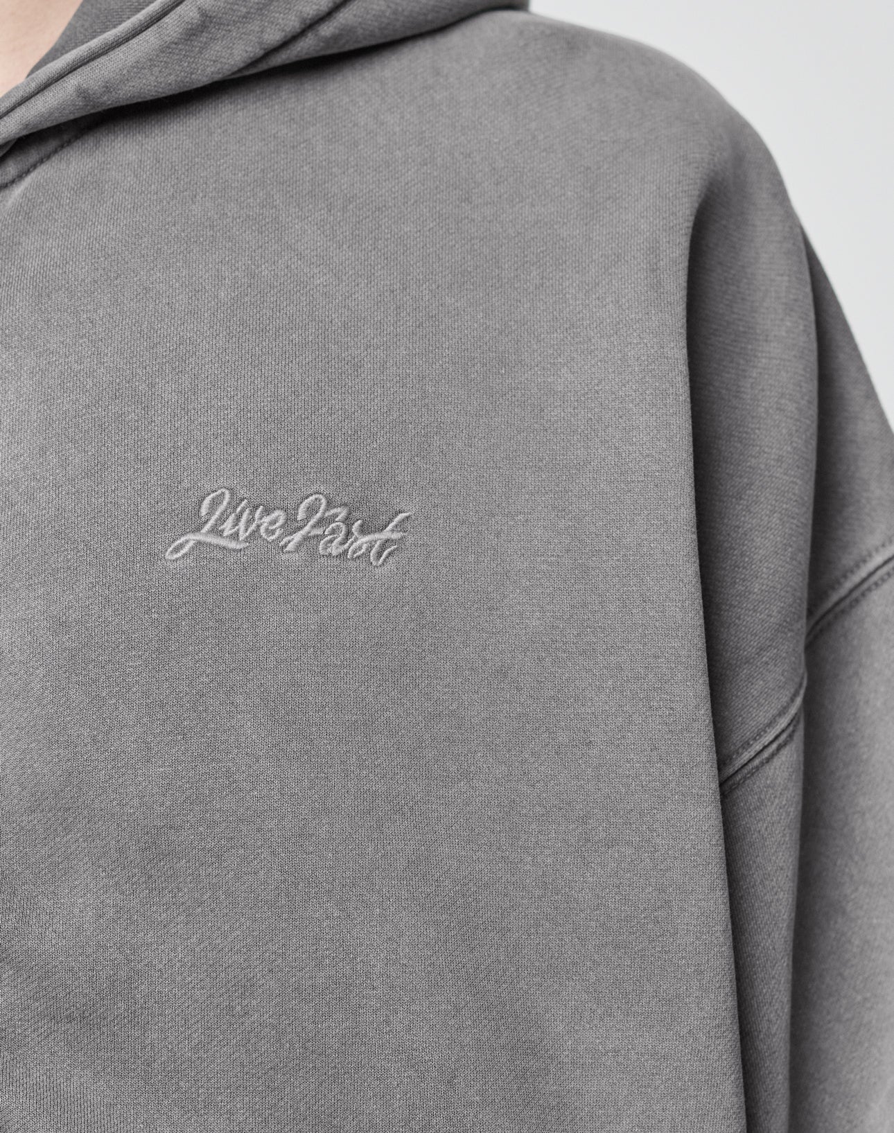 Close-up of the Basic Script Hooded Zip by LIVE FAST DIE YOUNG: a gray hoodie in soft cotton, featuring Live Fast embroidered in white cursive on the left chest and a subtly textured, vintage-inspired finish.