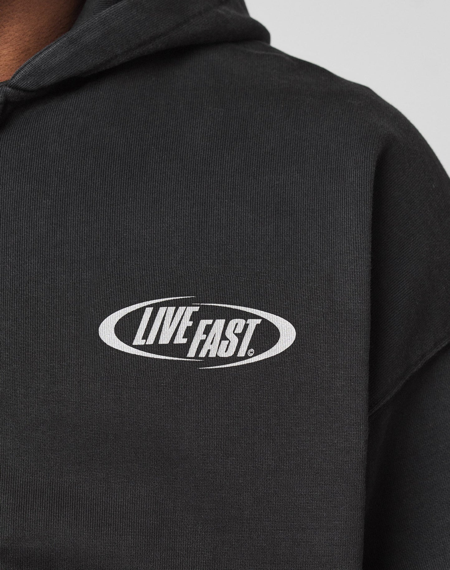 Close-up of the LFDY Canine Hooded Zip by LIVE FAST DIE YOUNG, a black oversize-fit hoodie in a Baumwolle-Polyester blend, featuring a white oval LIVE FAST! logo on the chest.