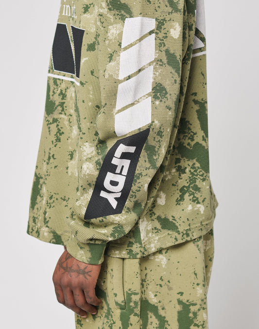 A person wears the LFDY Racing Waffle Longsleeve by LIVE FAST DIE YOUNG, featuring a green paint-splattered design with white stripes, bold front print, LF DY sleeve detail, and matching pants. Made from 100% Baumwolle in an oversize fit.